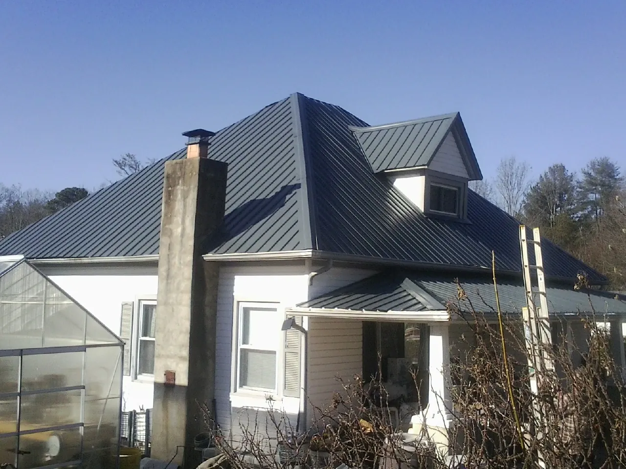 Dark blue standing seam metal roof on a white farmhouse with dormer — Slate & Tile Roof Repair by Roofing Brothers in Neola