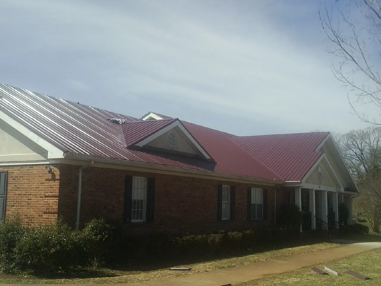 Red metal roof with gabled entries on a long brick building, from a Hail Damage Roof Repair job in Neola