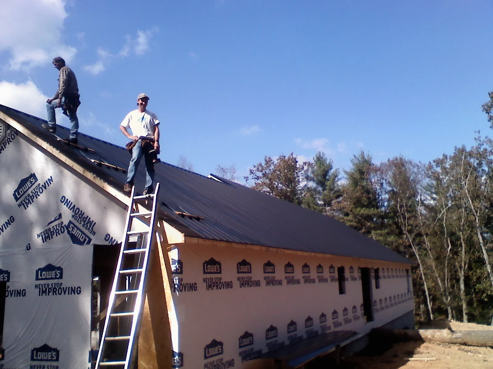 Two roofers standing on a long dark metal roof over a wrapped building in Neola