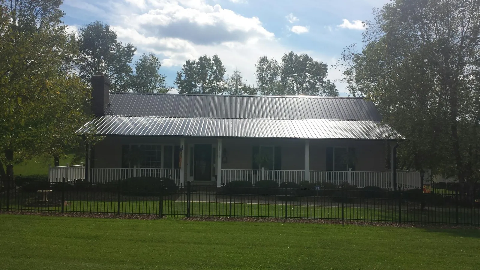 Gray metal roof on a brick ranch with a full width front porch — Gutter Guard Installation work by our crew in Neola